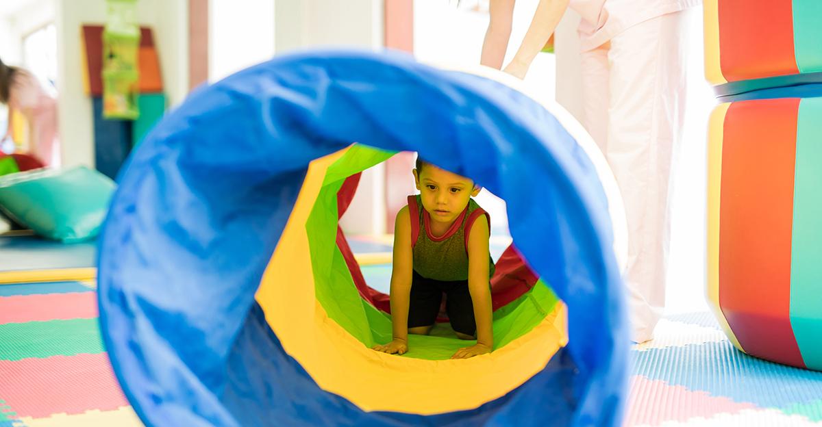 child playing and crawling through a colorful tunnel tube at a physical therapy center