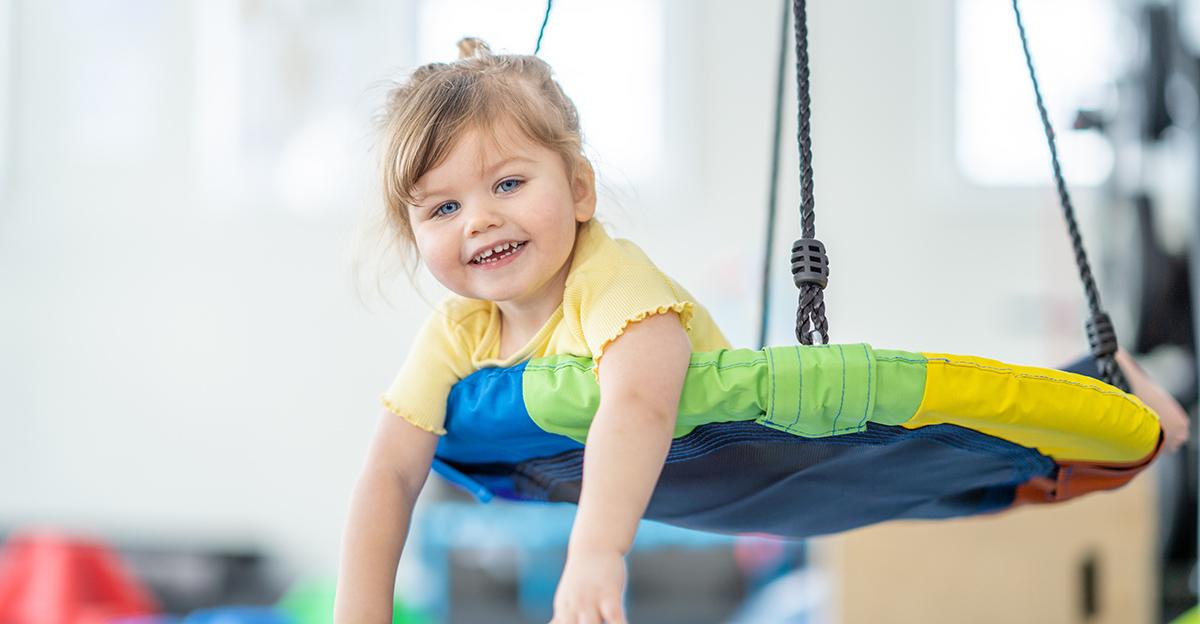 little girl smiling while laying on her stomach in a spinning sensory therapy swing