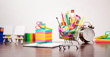 set of classroom school supplies on a wooden table, focus on a mini shopping cart filled with supplies