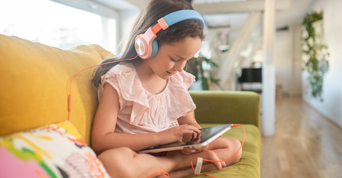 young girl on a couch wearing headphones and playing an educational game on a tablet