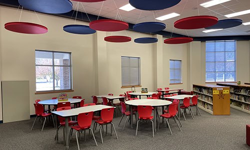 school multi-use space with cafeteria tables and chairs and shelves of books