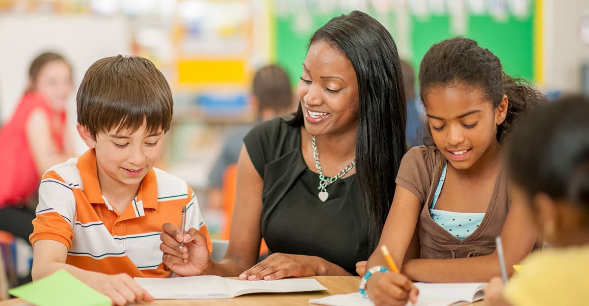 teacher assisting two students at a table