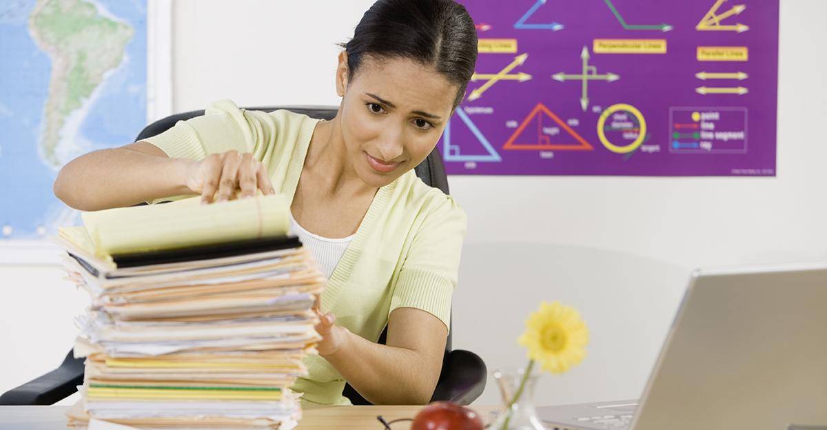 concerned female teacher looking at a tall stack of papers on her desk