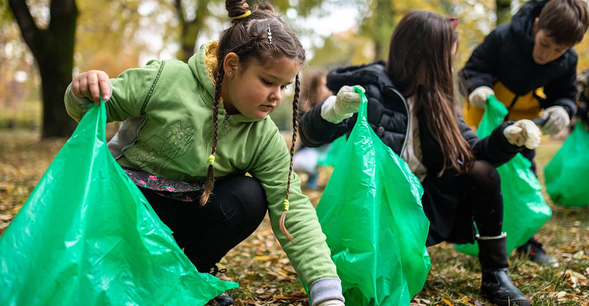 young students picking up garbage and putting it in green bags