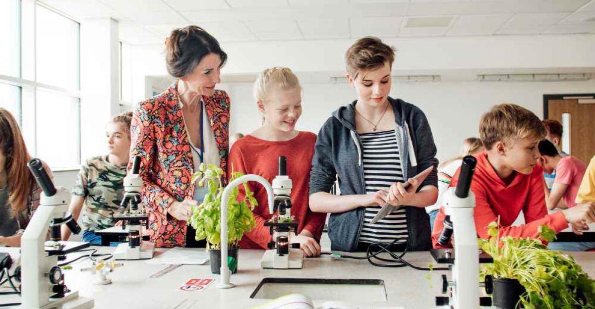 A teacher and hree students working with microscopes in a lab setting.