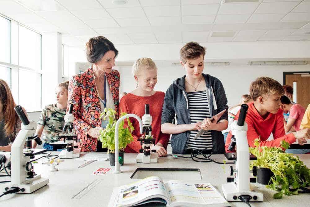 A teacher and hree students working with microscopes in a lab setting.