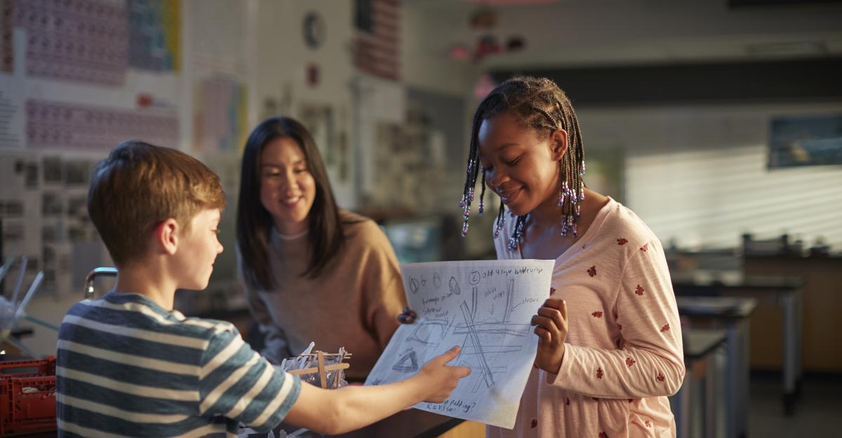 Two girls and a boy in a science classroom looking at a drawing.