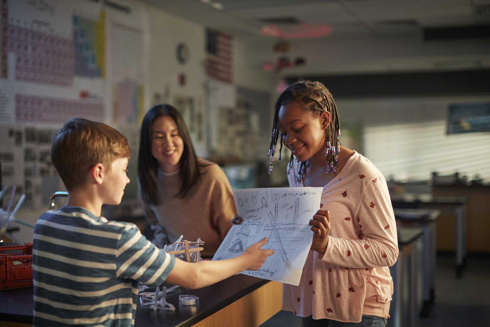 Two girls and a boy in a science classroom looking at a drawing.