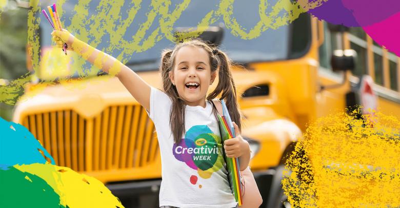 young girl with pigtails in front of a school bus holding colorful art supplies