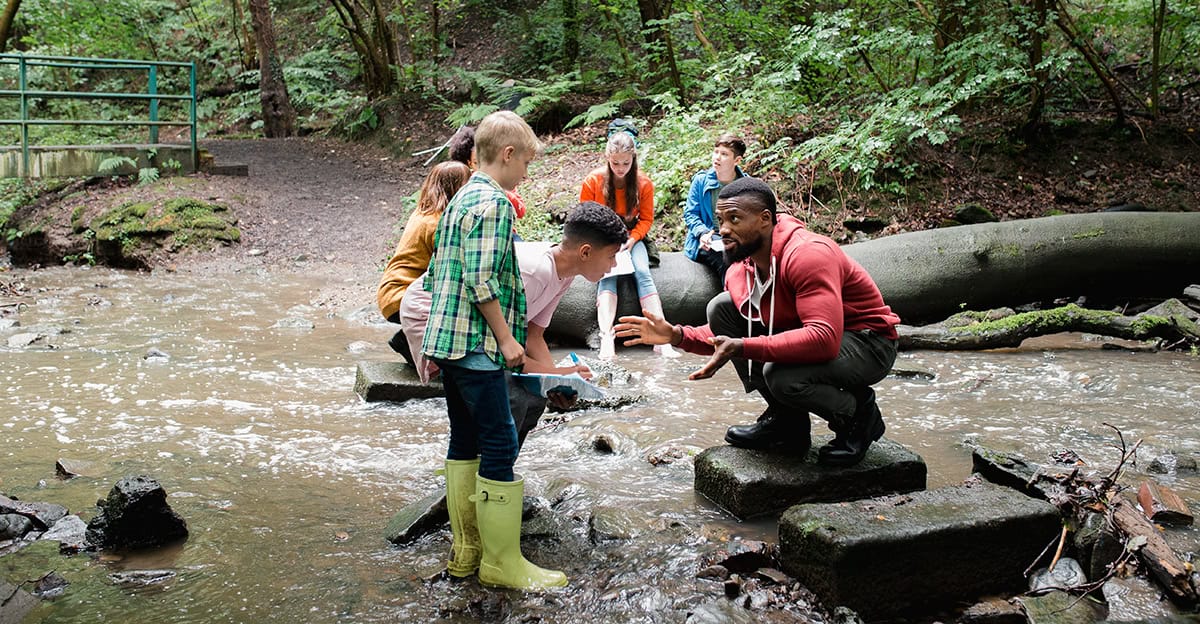 A teacher and group of students in a stream in the woods.