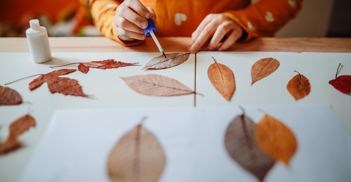 Girl child glues dried leaves on paper, children's creativity, seasonal crafts, and school tasks.