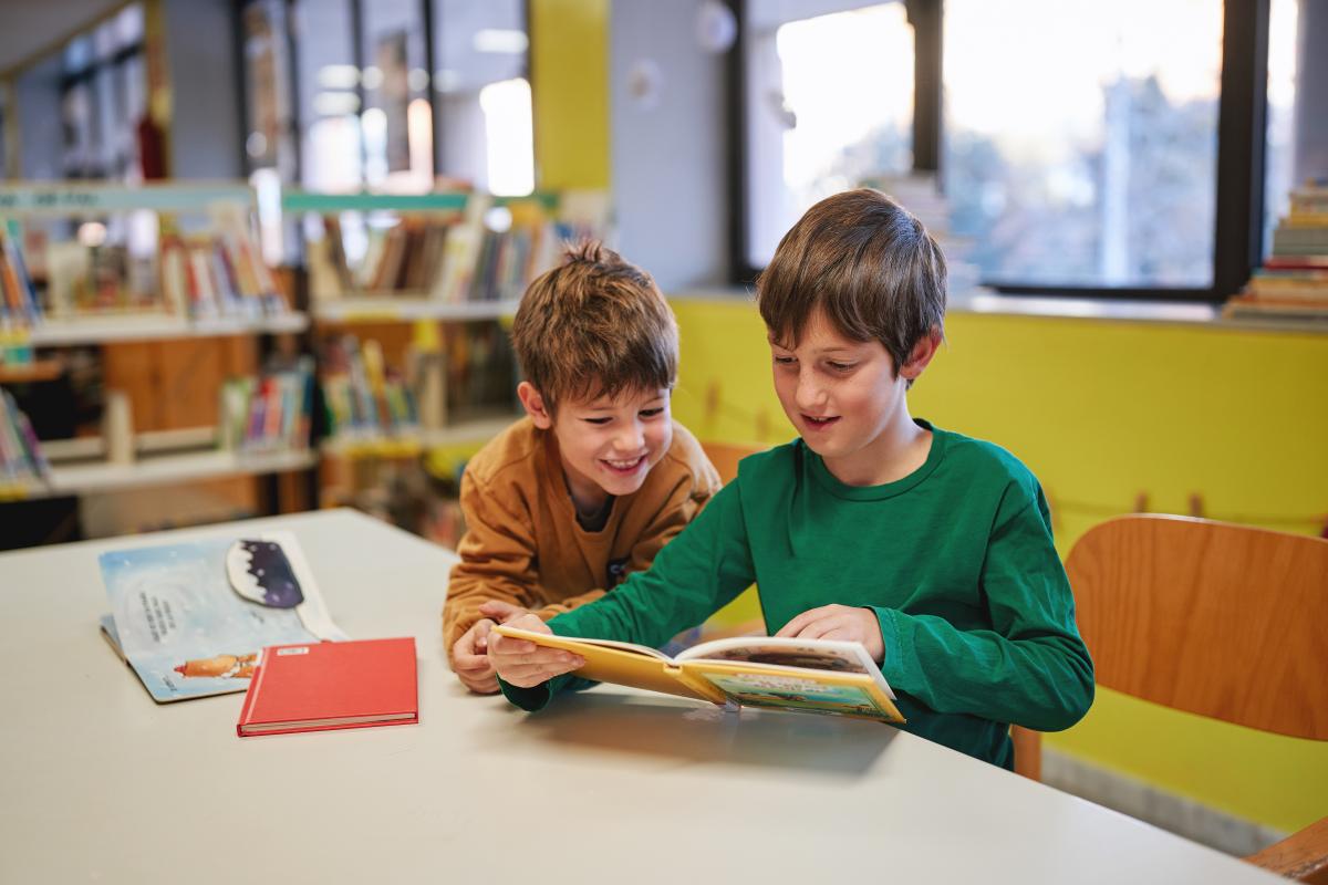 Two boys reading a book together in a library