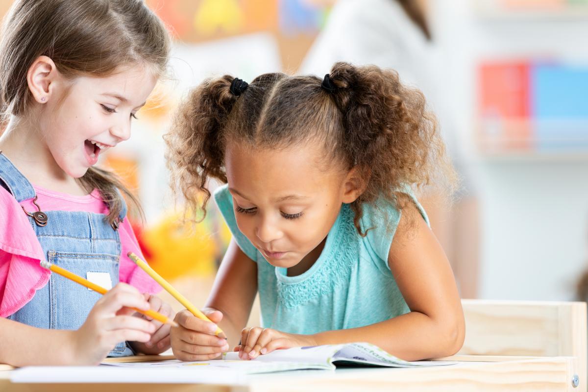 Two young girls focused on drawing and learning at a desk, demonstrating concentration and collaboration in an educational environment.