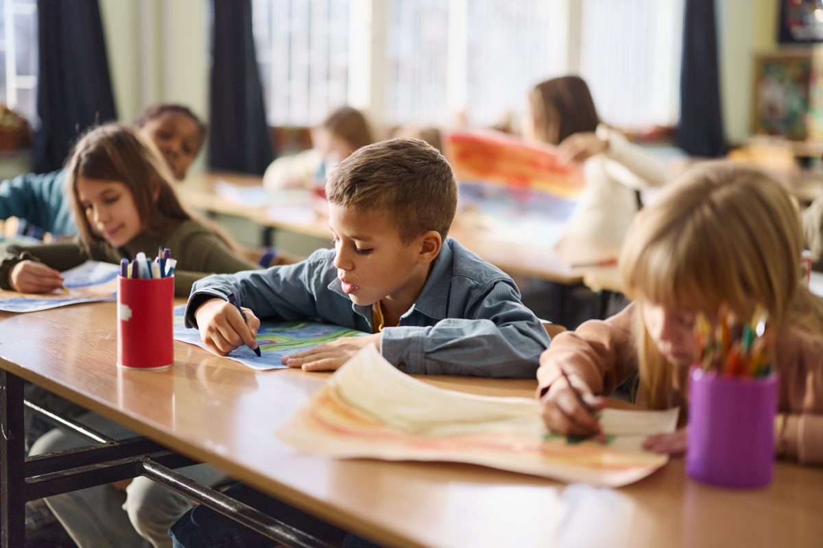 Grupo de alunos colorindo durante aula de artes no ensino fundamental. O foco está no garoto.