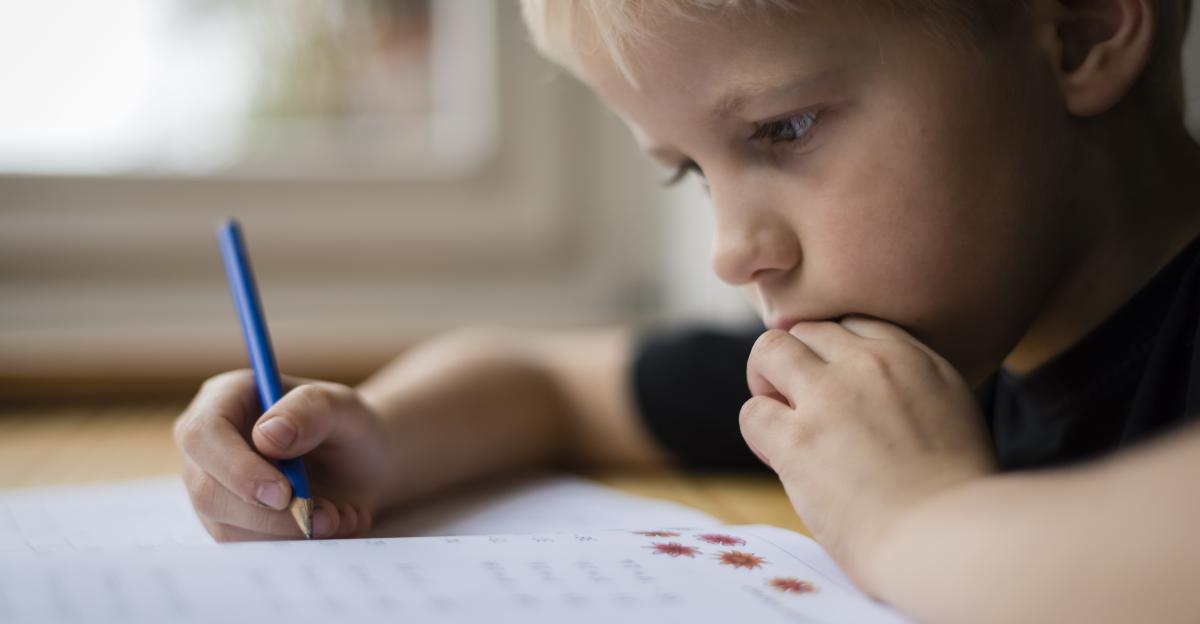 Portrait of a 9-year old caucasian boy sitting at home at his desk and doing his maths homework. Candid shot, natural light.