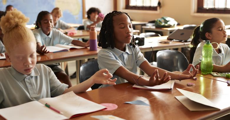 Group of multiracial students meditating while sitting at desks in classroom